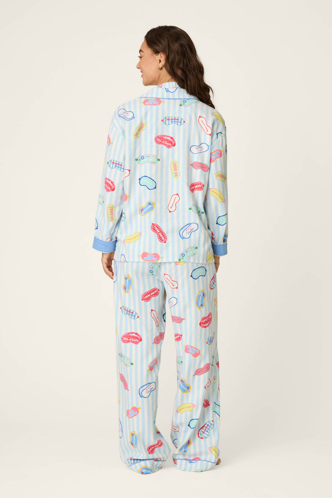 A woman stands facing away against a plain light background, wearing the P.J. Salvage Out of Office Eyemask Print 3-Piece Flannel PJ Set featuring a colorful lips and toothbrush pattern in light blue.