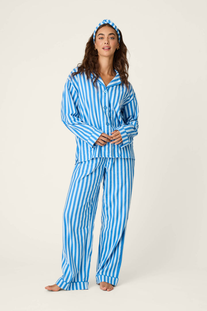 A woman wears the P.J. Salvage Snowflake Icon 3-Piece Long Sleeve Flannel PJ Set—featuring blue and white stripes with a matching headband—standing barefoot against a plain light background.