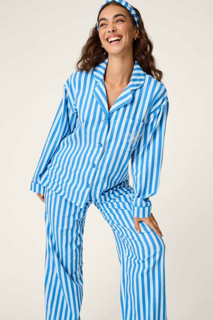A woman smiles and poses in the P.J. Salvage Snowflake Icon 3-Piece Long Sleeve Flannel PJ Set, featuring blue and white stripes with a matching headband, against a plain background.