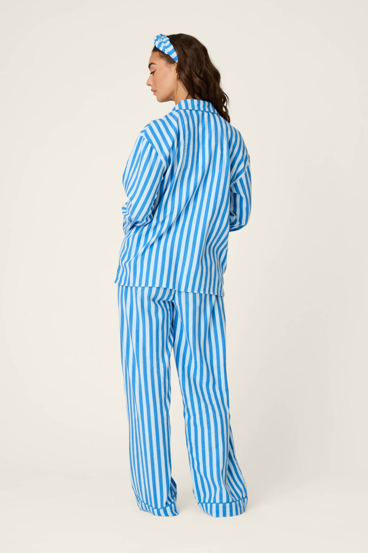 A woman facing away is wearing the P.J. Salvage Snowflake Icon 3-Piece Long Sleeve Flannel PJ Set, featuring blue and white vertical stripes with a matching headband, standing against a plain light background.