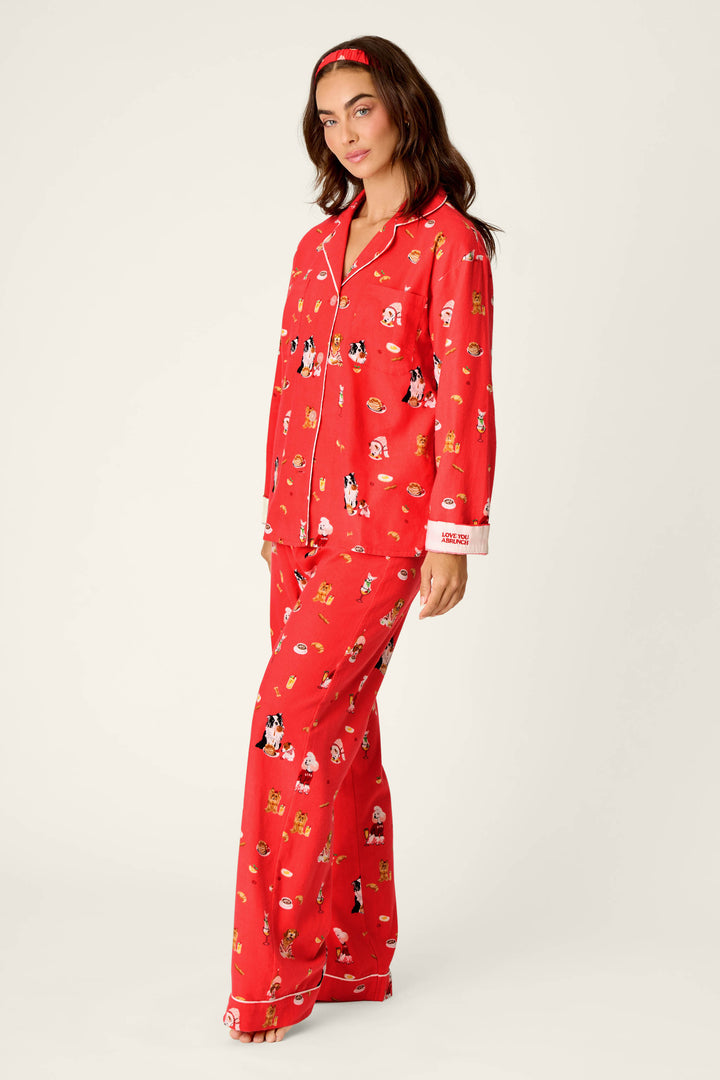 A woman wearing the P.J. Salvage Dogs Who Brunch Print 3-Piece Long Sleeve Flannel PJ Set, featuring playful cartoon prints and a matching headband, stands with one leg forward and a soft smile against a plain light background.