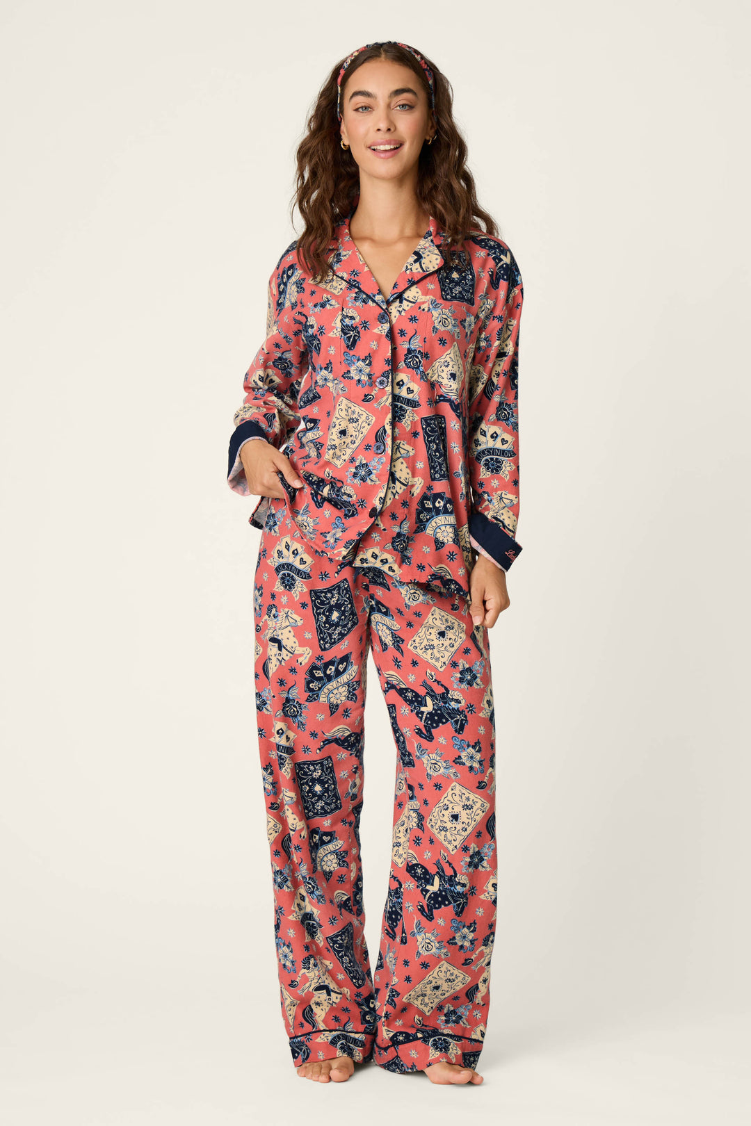 A woman stands barefoot against a plain light background, wearing the P.J. Salvage Lucky in Love Western Print 3-Piece Long Sleeve Flannel PJ Set, which features coordinating pink flannel pajamas with blue and cream floral and bandana prints, along with a matching headband.