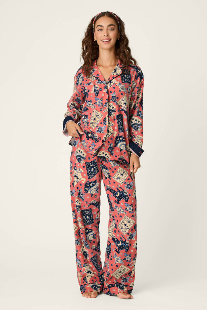 A woman stands barefoot against a plain light background, wearing the P.J. Salvage Lucky in Love Western Print 3-Piece Long Sleeve Flannel PJ Set, which features coordinating pink flannel pajamas with blue and cream floral and bandana prints, along with a matching headband.