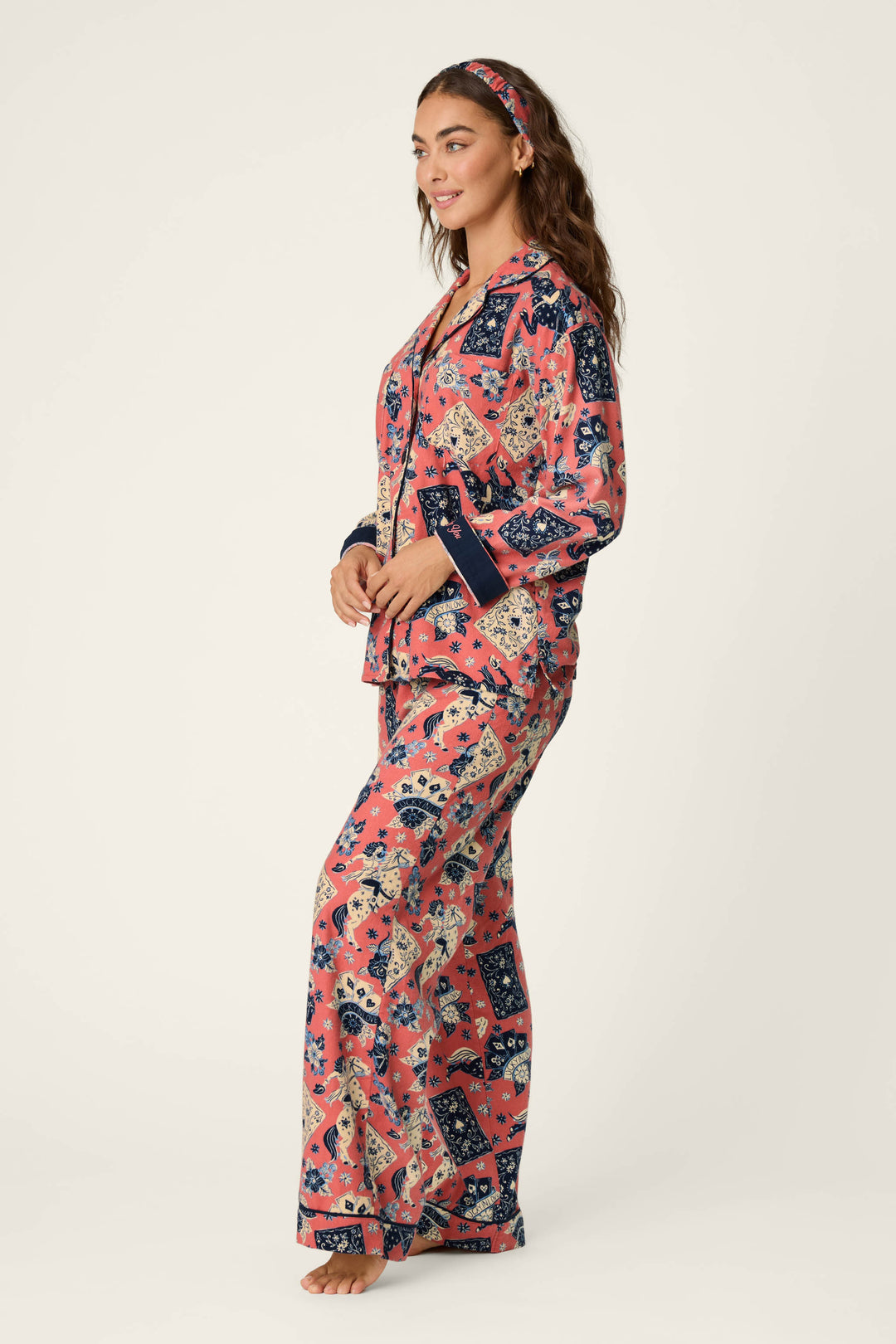 A woman stands sideways, smiling and barefoot against a plain light background, dressed in the P.J. Salvage Lucky in Love Western Print 3-Piece Long Sleeve Flannel PJ Set—a coordinated ensemble featuring a vibrant western-inspired print and a matching headband.