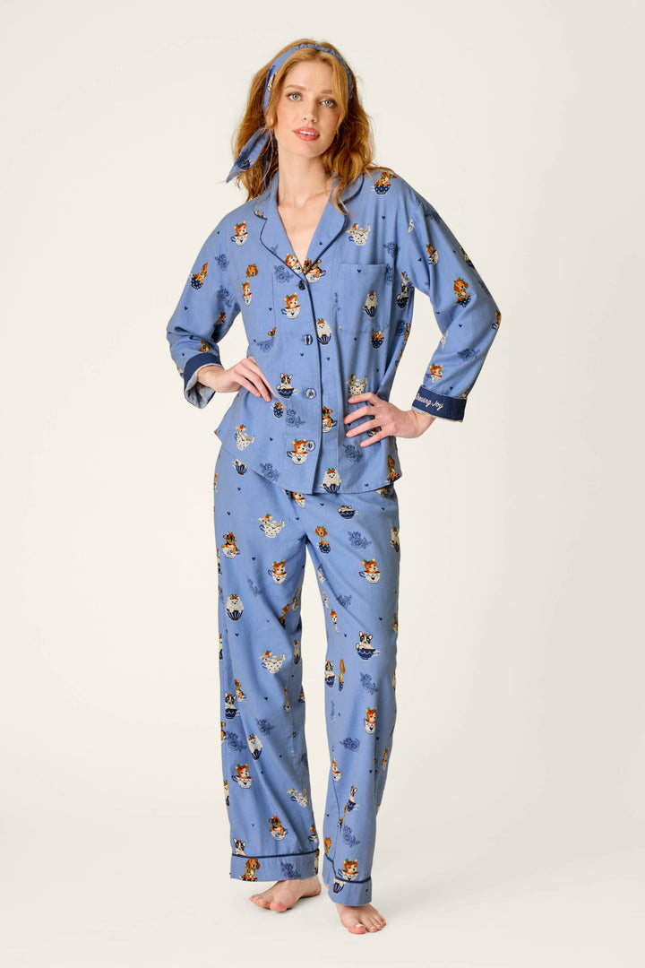 A woman stands barefoot on a plain background wearing the P.J. Salvage Teacup Pups 3-Piece Flannel PJ Set, featuring a charming animal print and a matching blue headband, with one hand resting on her hip.