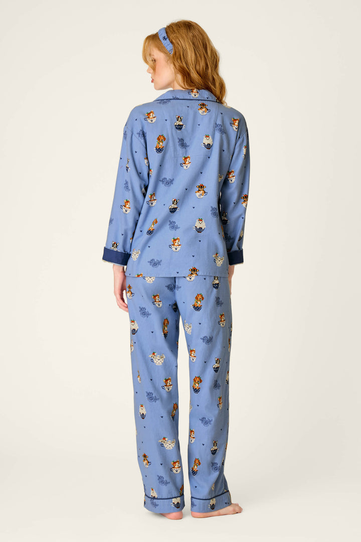 A person with long hair is seen from behind wearing the P.J. Salvage Teacup Pups 3-Piece Flannel PJ Set—blue pajamas featuring a cartoon dog print—with bare feet and a matching blue headband, against a simple light background.