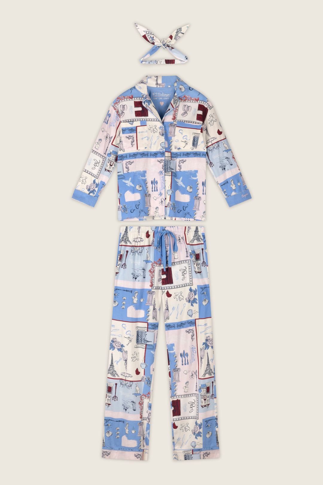 The P.J. Salvage Allons-y Parisian Print 3-Piece Flannel PJ Set includes women's pajamas and a coordinating headband, featuring a collared button-up top and drawstring pants in a blue, pink, and white patchwork print with whimsical illustrations.