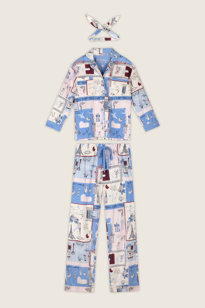 The P.J. Salvage Allons-y Parisian Print 3-Piece Flannel PJ Set includes women's pajamas and a coordinating headband, featuring a collared button-up top and drawstring pants in a blue, pink, and white patchwork print with whimsical illustrations.