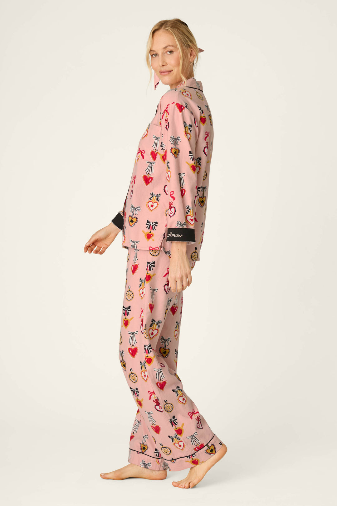A woman stands barefoot wearing the Love Lockets Print 3-Piece Long Sleeve Flannel PJ Set by P.J. Salvage, featuring colorful and playful prints. She is turned slightly to the side with a soft smile, her blonde hair loosely tied back, against a plain light background.