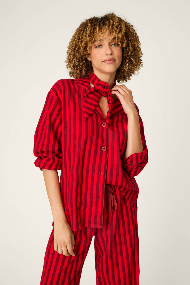 A person with curly hair wears the P.J. Salvage Bow Icon 3-Piece Long Sleeve Flannel PJ Set, standing against a light background and gently holding the collar while smiling softly.