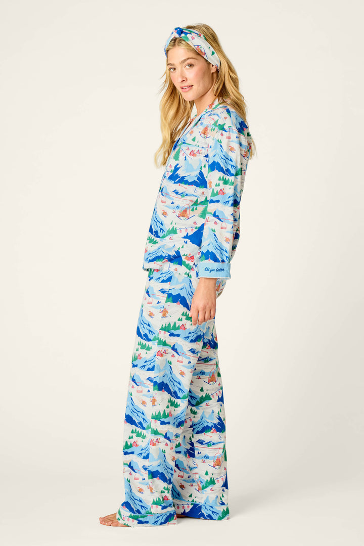 A woman stands barefoot in the P.J. Salvage Ski Ya Later Skiing Bears Print 3-Piece Flannel PJ Pant Set, featuring a matching pajama set and headband with a playful skiing bear print on a white background. She is turned slightly to the side and smiling gently.