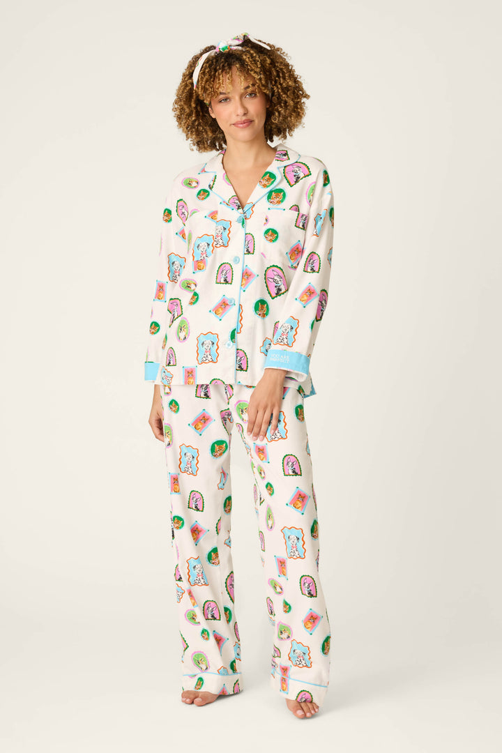 A person is standing barefoot against a plain light background, wearing the P.J. Salvage "Picture Purrfect Pet Portraits" 3-Piece Flannel PJ Set, featuring matching white pajamas adorned with colorful cartoon food prints, light blue trim, and a coordinating headband.