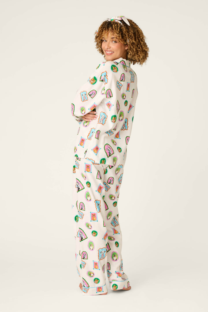 A person with curly hair smiles and poses sideways, wearing the P.J. Salvage Picture Purrfect Pet Portraits 3-Piece Flannel PJ Set—white pajamas adorned with colorful cat and food illustrations, paired with a matching headband—against a plain light background.