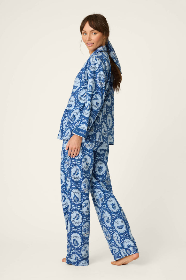 A woman wears the P.J. Salvage Fruit Medley Print 3-Piece Flannel PJ Set, featuring playful fruit-themed patterns, as she stands barefoot on a light background, turning slightly to the side and glancing over her shoulder.