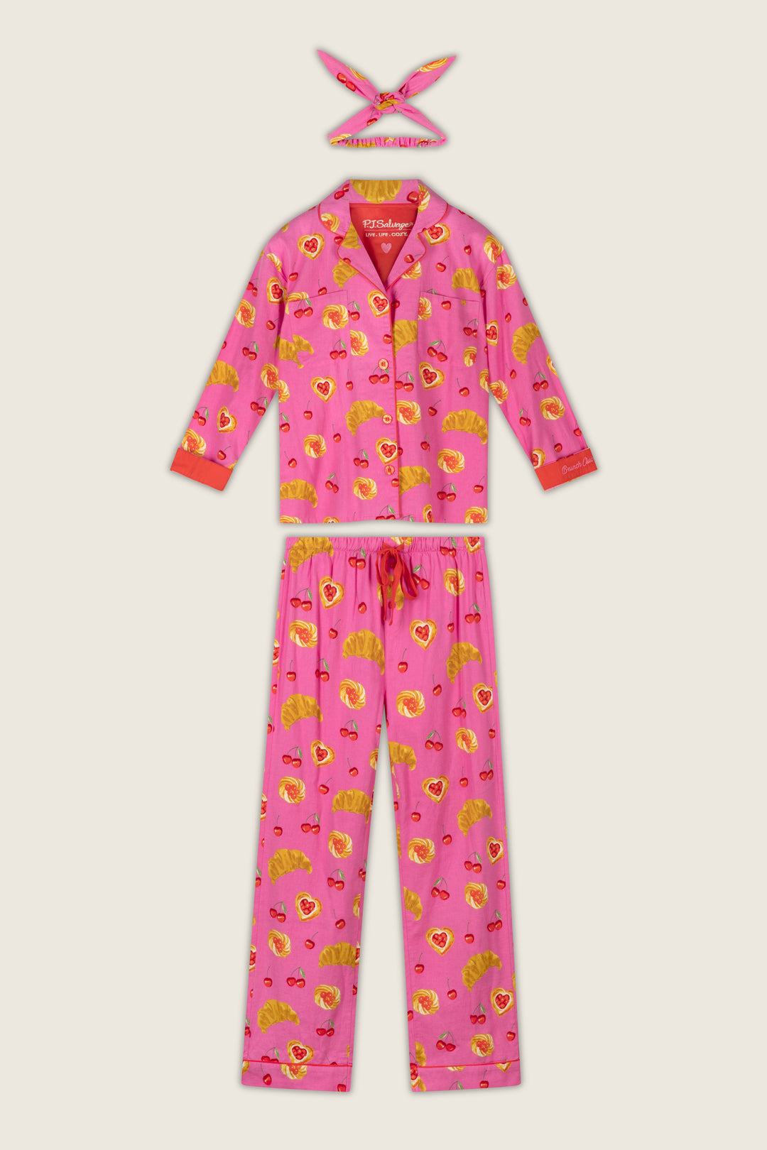 The Breakfast Pastry Print 3-Piece Flannel PJ Set by P.J. Salvage features a vibrant pink color with croissant and strawberry prints, including a button-up long-sleeve top, long drawstring-waist pants, and a matching headband.