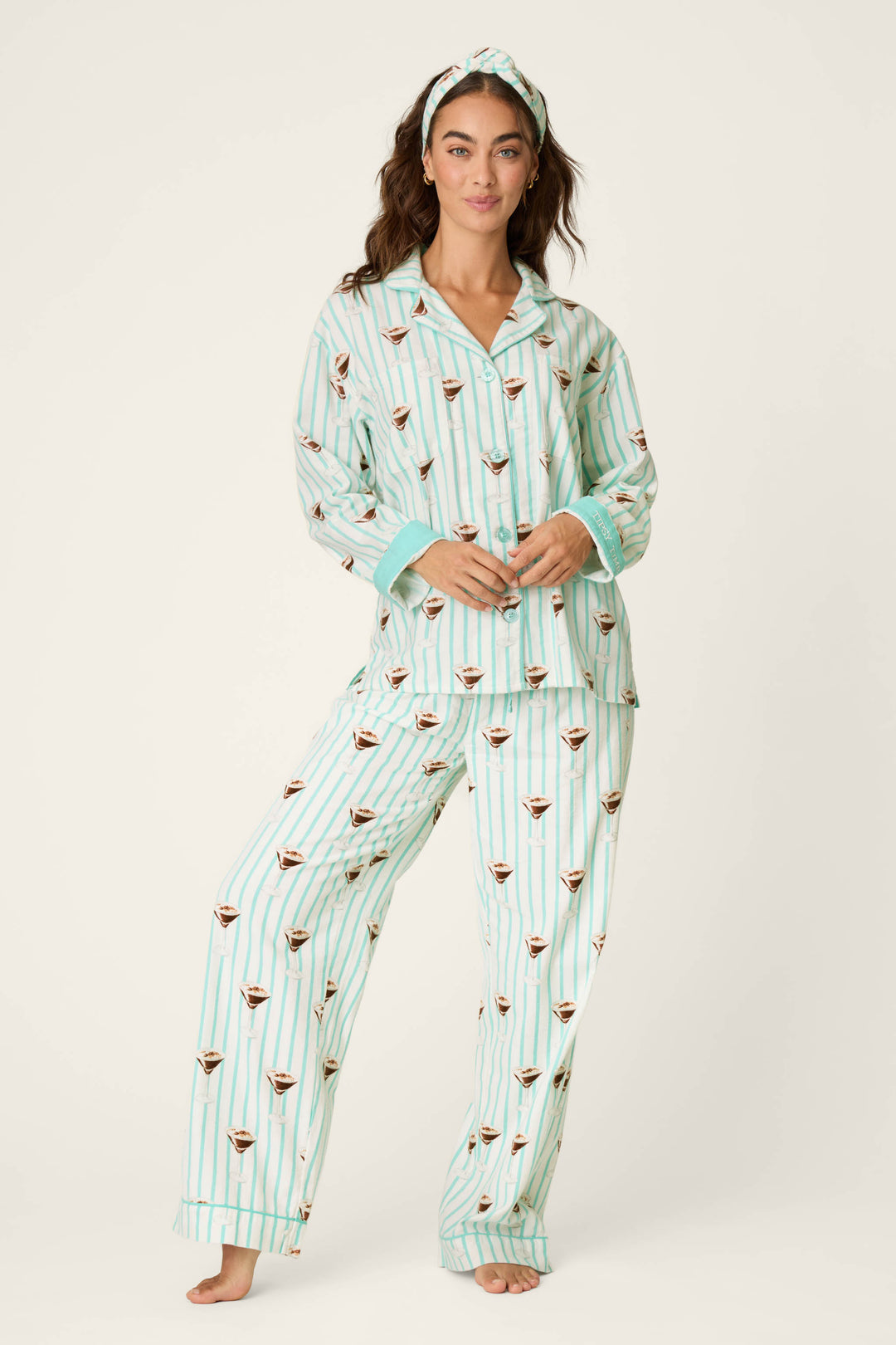A woman stands barefoot against a plain background wearing the P.J. Salvage Espresso Martini Print 3-Piece Long Sleeve Flannel PJ Set, featuring matching striped pajamas adorned with an espresso martini pattern and a coordinating headband.