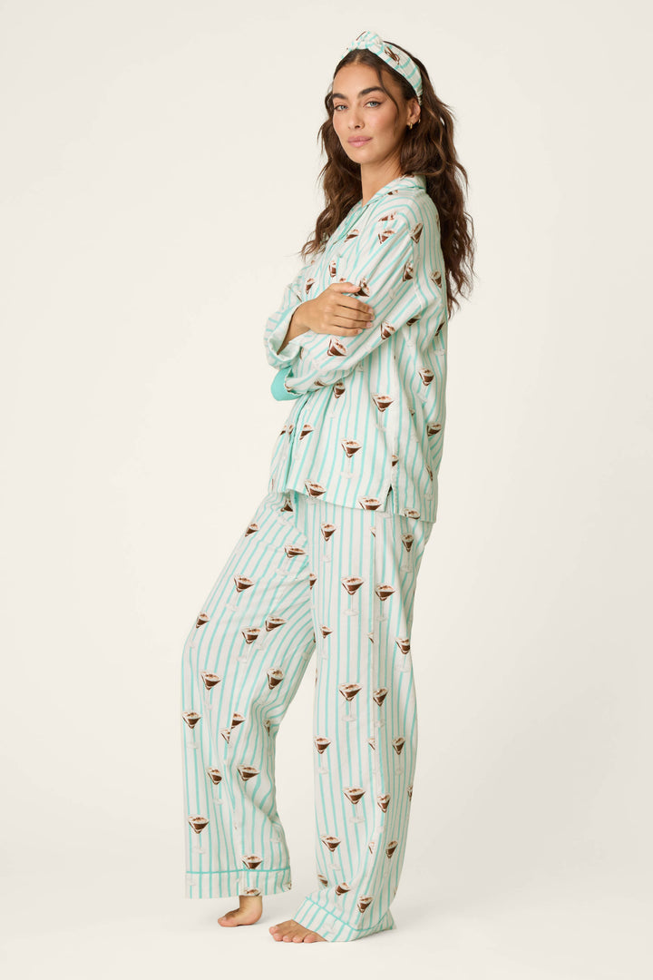 A woman stands barefoot wearing the P.J. Salvage Espresso Martini Print 3-Piece Long Sleeve Flannel PJ Set, which features matching striped pajamas with a playful cocktail print and a coordinated headband. She has long, wavy hair and crosses her arms, looking confidently at the camera against a plain background.