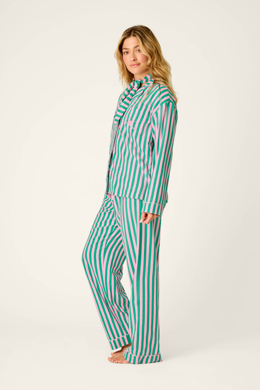 A woman stands barefoot, wearing the P.J. Salvage Ski Bunny Icon 3-Piece Long Sleeve Flannel PJ Set featuring matching vertical pink and green stripes, looking at the camera against a plain light background.