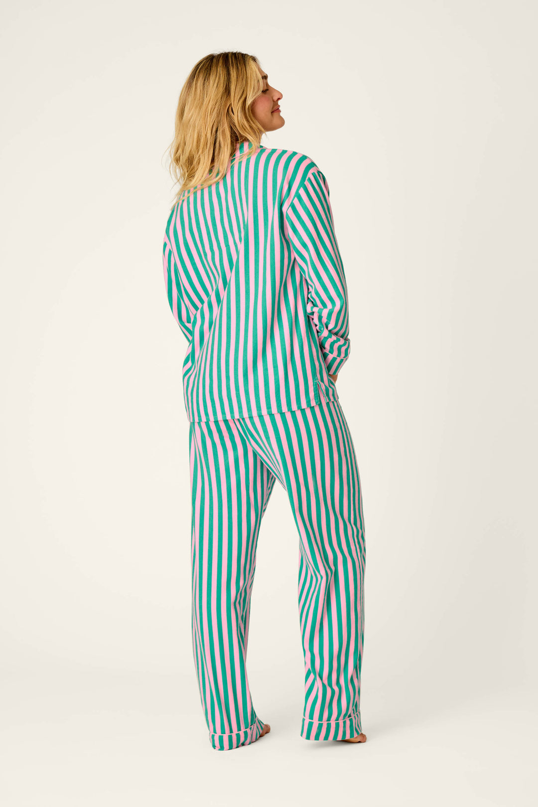 A person stands facing away against a plain light background, wearing the P.J. Salvage Ski Bunny Icon 3-Piece Long Sleeve Flannel PJ Set, which features matching vertical green, pink, and white stripes.