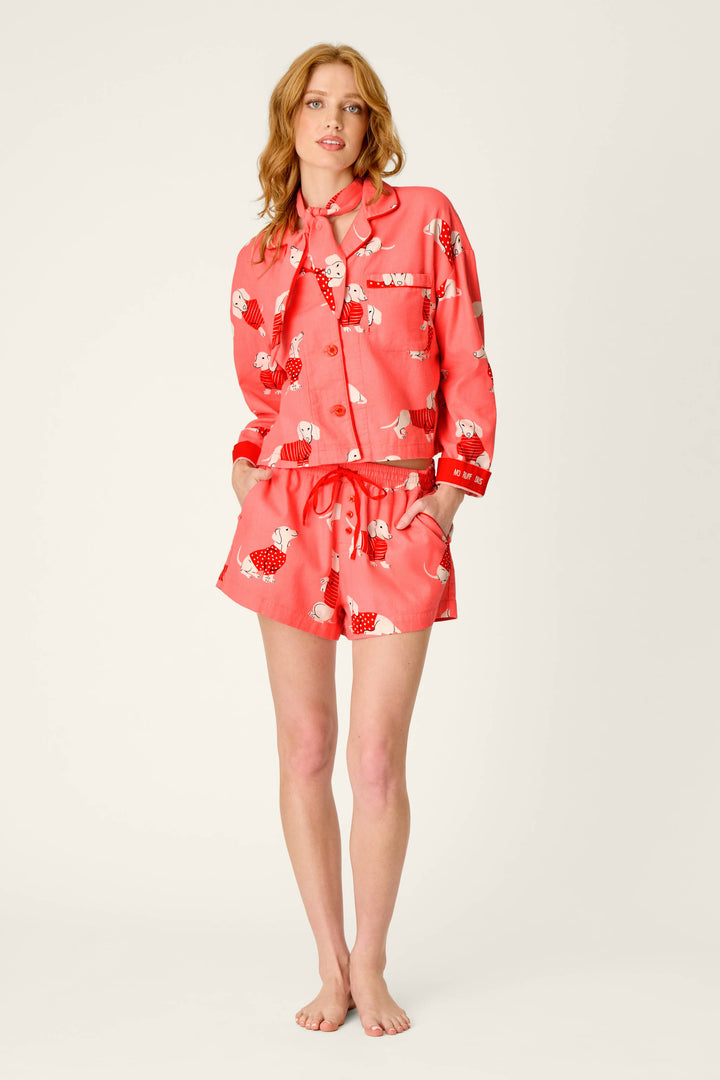 A person stands barefoot wearing the P.J. Salvage Dachshund Print 3-Piece Short Flannel PJ Set, which includes a matching button-up top and shorts featuring a whimsical dachshund print. The background is plain and light-colored.