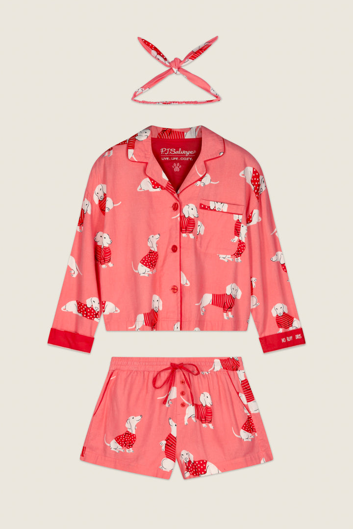 The P.J. Salvage Dachshund Print 3-Piece Short Flannel PJ Set, featuring a pink long-sleeve button-up top, drawstring shorts, and a matching headband, is displayed flat on a light background.