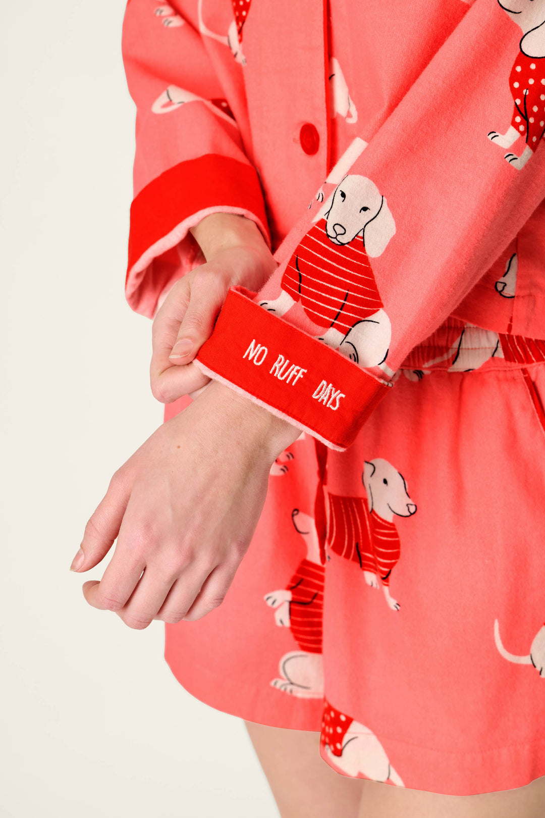 Wearing the P.J. Salvage Dachshund Print 3-Piece Short Flannel PJ Set, a person rolls up their sleeve to reveal white “NO RUFF DAYS” text on the red cuff.