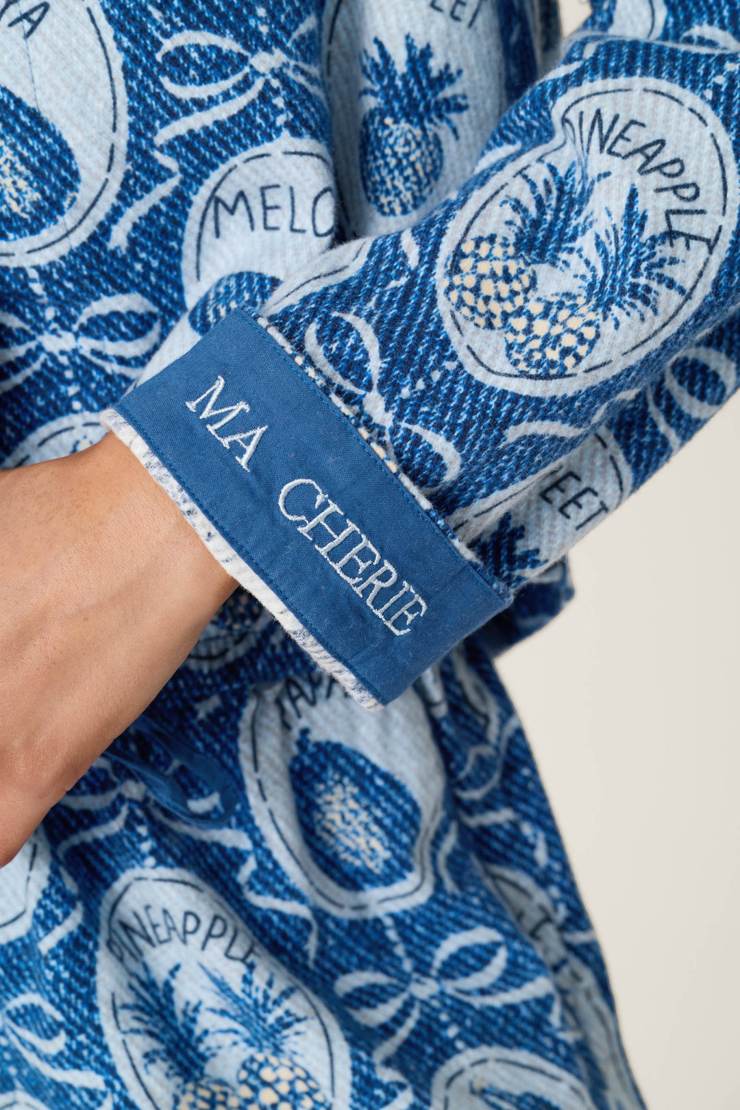 A close-up of the Fruit Medley Print 3-Piece Short Flannel PJ Set by P.J. Salvage shows a blue patterned sleeve featuring pineapples, the words "pineapple" and "melon," and a cuff embroidered with "MA CHÉRIE" in white.