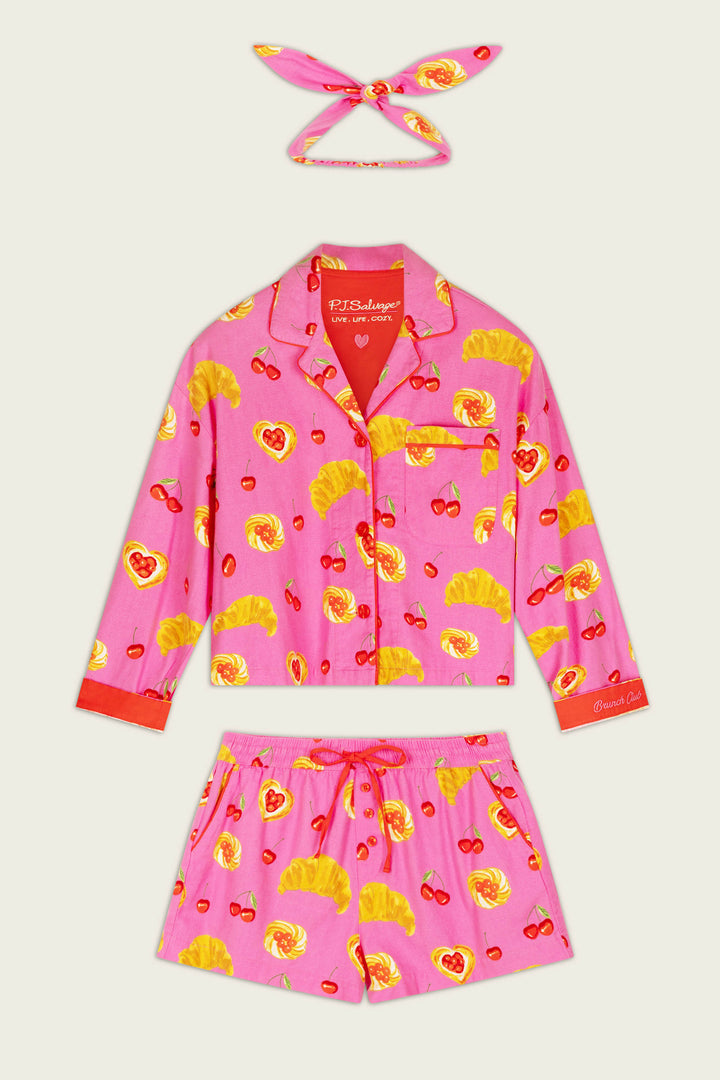 The Breakfast Pastry Print 3-Piece Short Flannel PJ Set by P.J. Salvage includes a bright pink long-sleeve button-up top, drawstring shorts, and a matching headband, all adorned with charming croissant, cherry, and heart motifs.