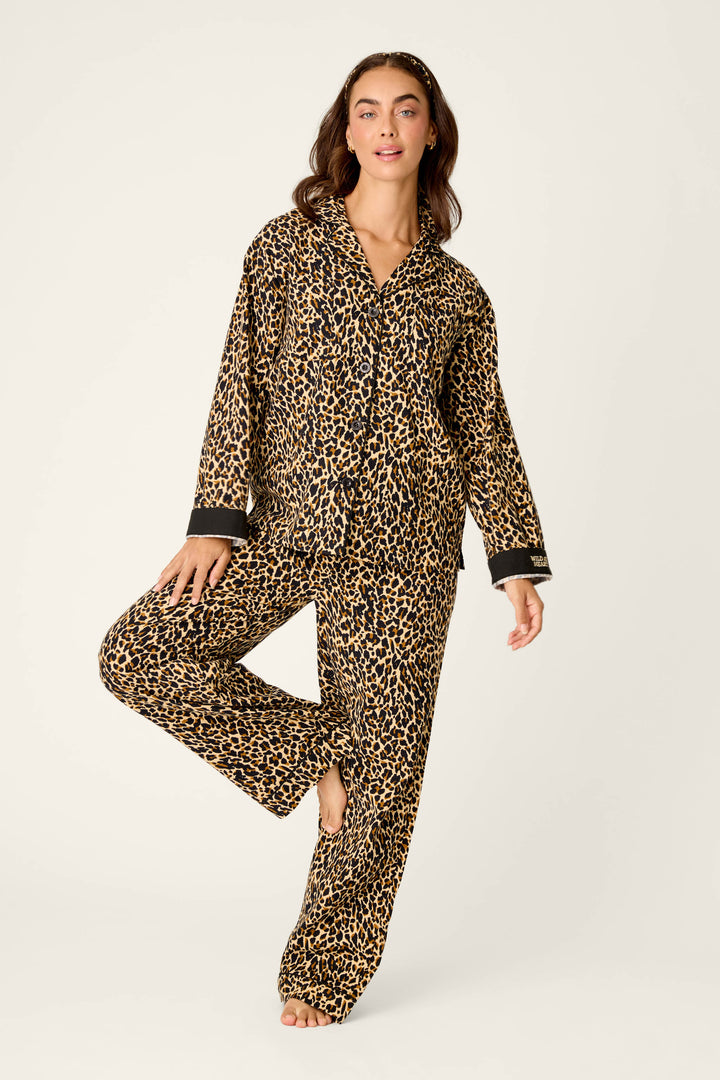 A woman models the P.J. Salvage Wild At Heart Leopard Print 3-Piece Flannel PJ Set, standing on one leg with the other leg bent, arms relaxed at her sides, and smiling against a plain light-colored background.