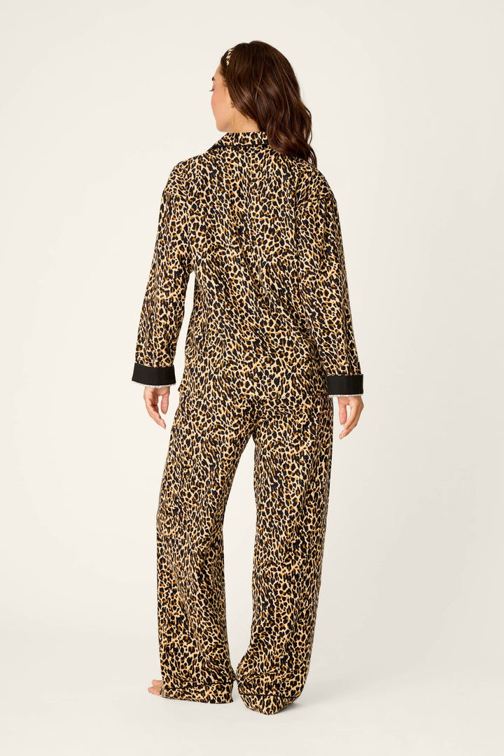 A person stands barefoot facing away from the camera, wearing the P.J. Salvage Wild At Heart Leopard Print 3-Piece Flannel PJ Set, which features loose-fitting, long-sleeved pajamas with a leopard print pattern on a light background.