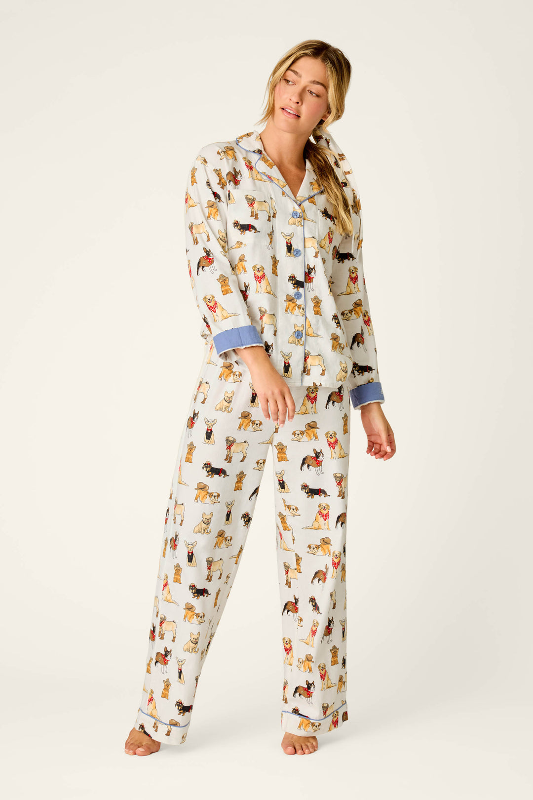 A woman stands barefoot in the P.J. Salvage Howdy Pup-ner Dog Print 3-Piece Flannel PJ Set, featuring blue cuffs, gazing to the side against a plain light background.
