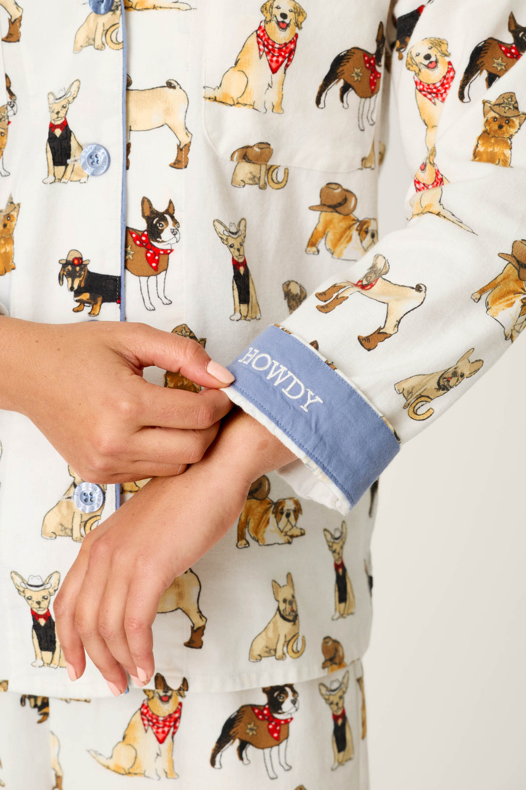 A person wearing the P.J. Salvage Howdy Pup-ner Dog Print 3-Piece Flannel PJ Set points to the blue cuff of their sleeve, which has “HOWDY” embroidered on it in white letters.