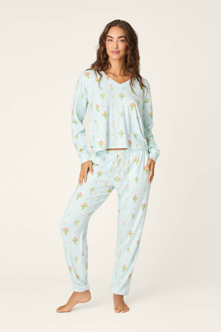 A woman with long wavy hair stands barefoot in P.J. Salvage’s Feelin' Prickly Cactus Blooms Long Sleeve Top pajamas, featuring a cactus print pointelle top and drawstring pants—perfect for cozy nights and a relaxed vibe.