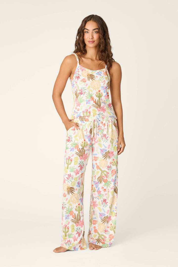 A woman stands barefoot in the P.J. Salvage Feelin' Prickly Desert Dreams Long PJ Set, a sleeveless, loose-fit pajama with colorful desert botanicals and cacti on white, hands in pockets against a plain light background.