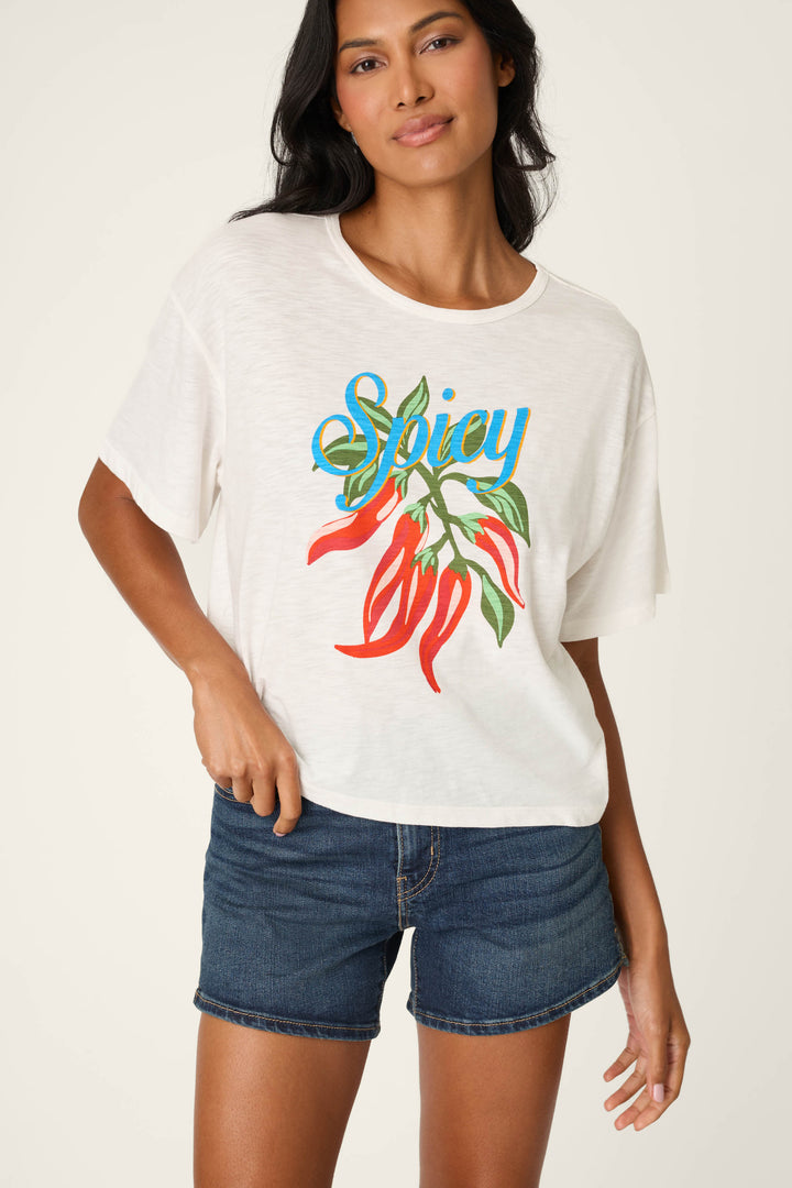 A woman wearing the P.J. Salvage Feelin’ Prickly Spicy Chili Graphic T-Shirt and dark denim shorts stands against a plain light background, smiling confidently.