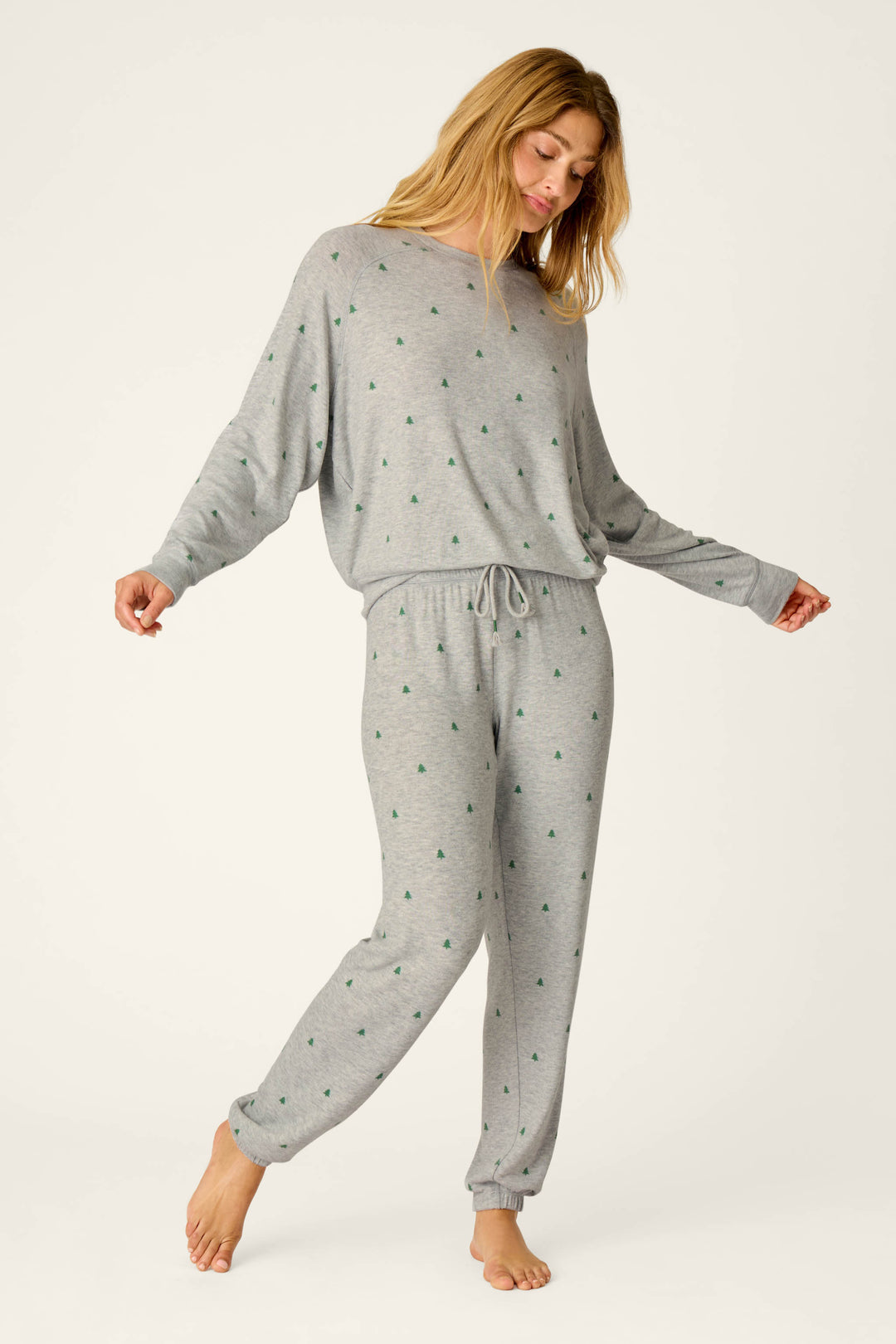 Wearing the P.J. Salvage Happy Campawr Tree Print Long Sleeve Top, a woman stands barefoot on one leg with arms slightly extended and head tilted to the side, set against a plain white background.