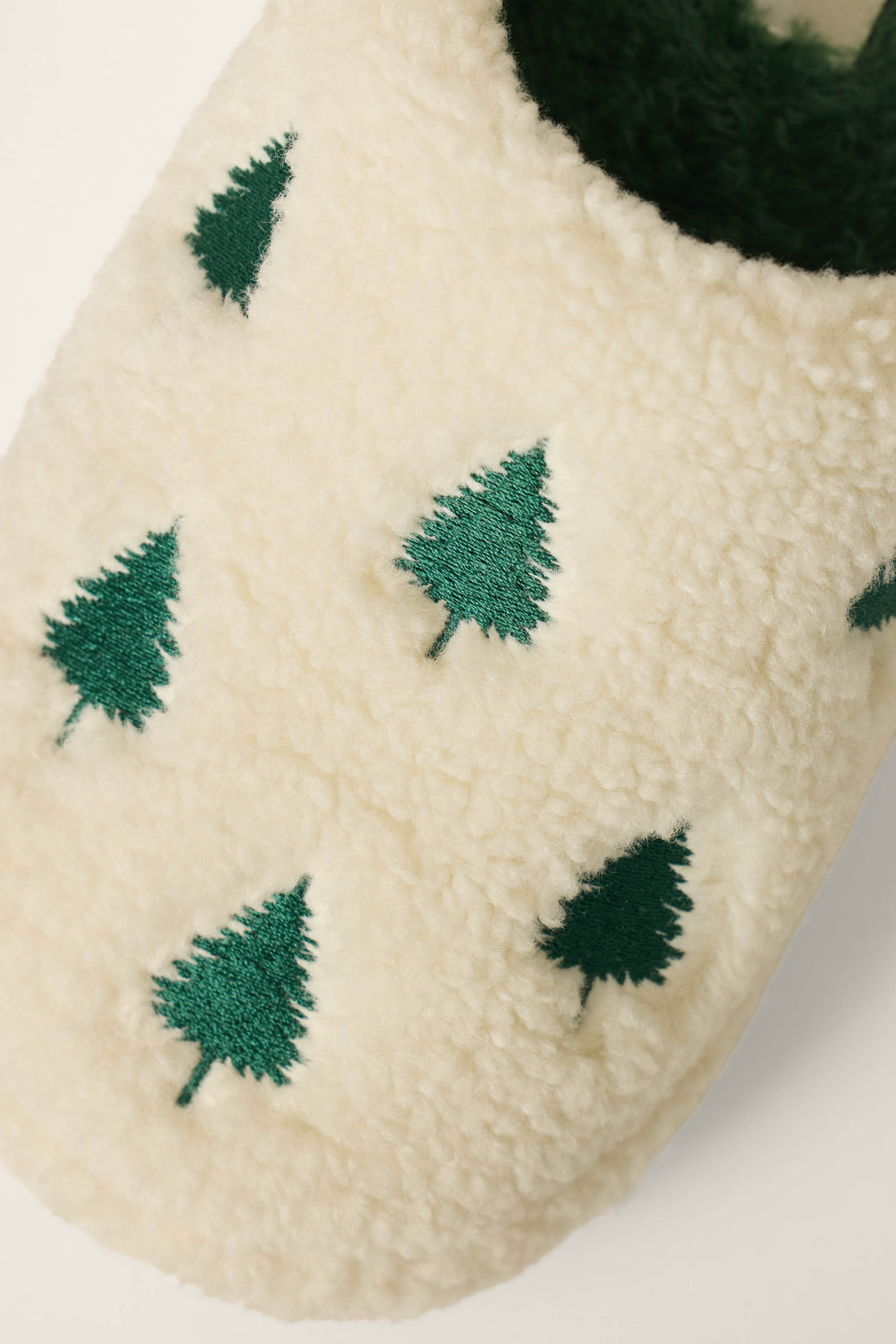 Close-up of the P.J. Salvage Tree Print Faux Sherpa Slippers, featuring a cream-colored faux sherpa texture with green embroidered pine trees highlighting the cozy design.