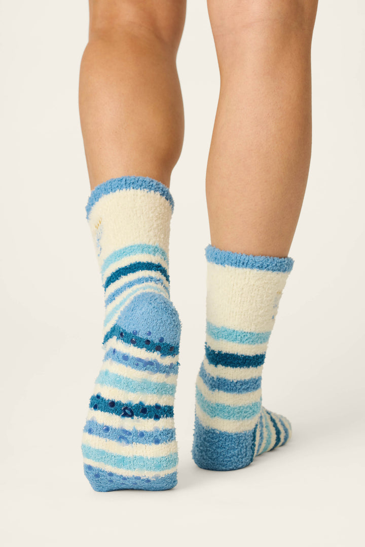 A person wears P.J. Salvage Hannukah Blue Stripe & Menorah Crew Socks, standing on a white background with only their lower legs and feet visible from the back.