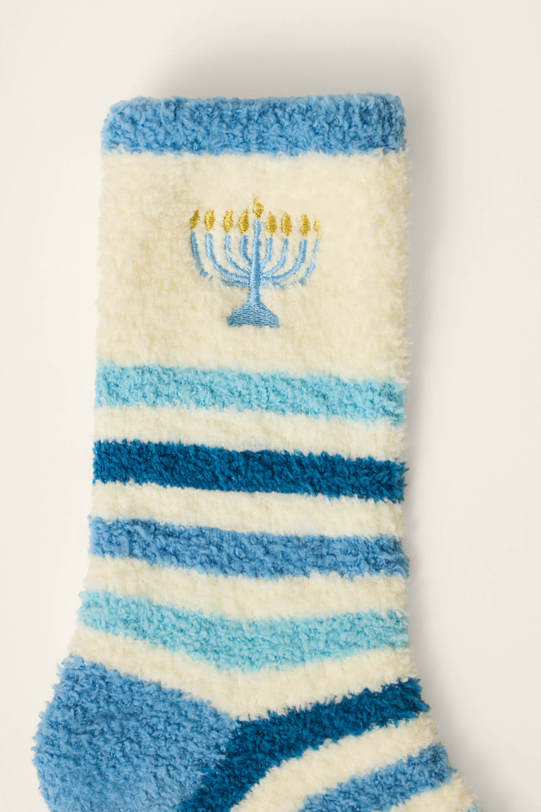 The P.J. Salvage Hannukah Blue Stripe & Menorah Crew Socks are fuzzy socks with blue and white stripes, featuring an embroidered menorah with lit candles near the top.
