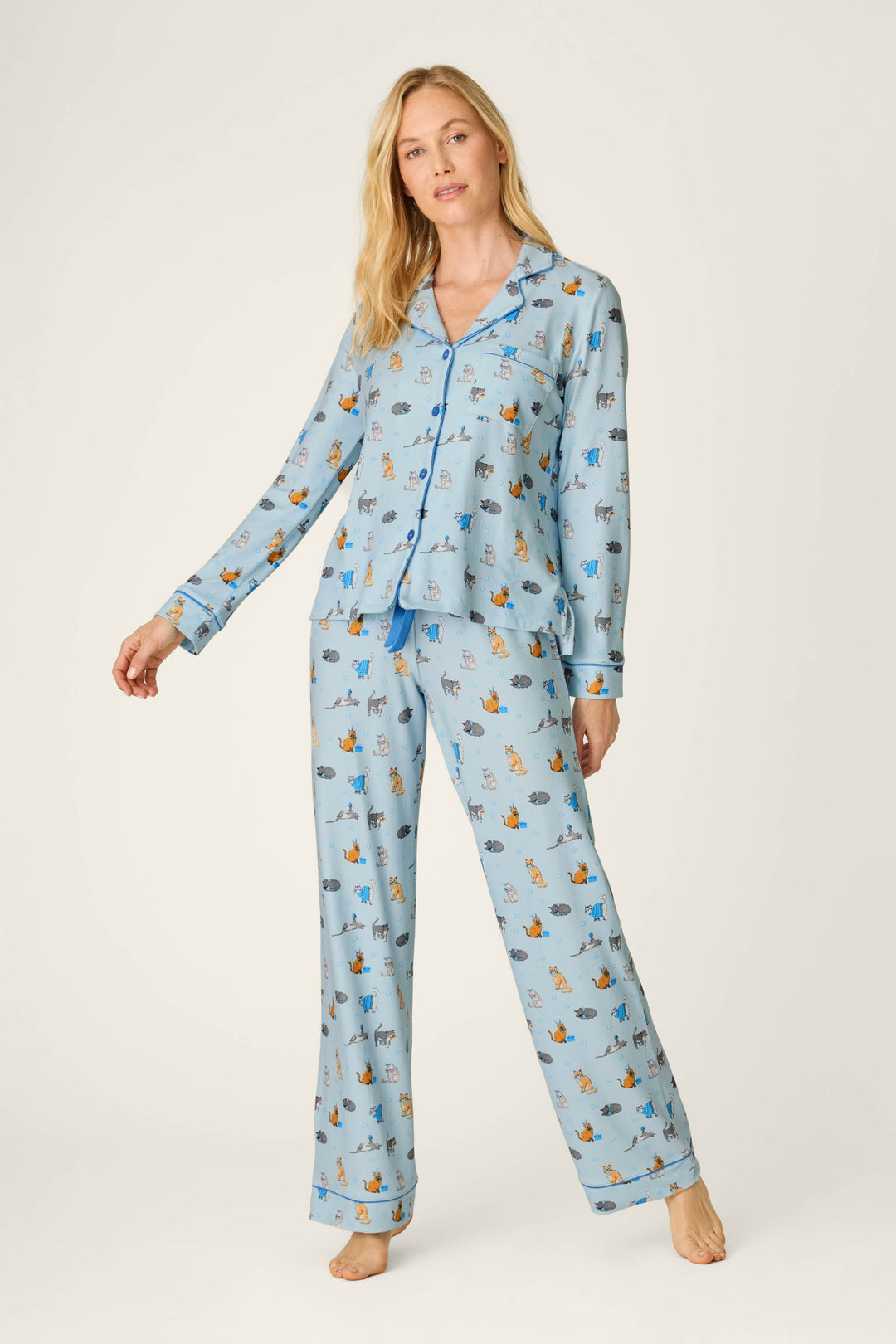 A woman wearing the Hanukkatz Paws for Celebration Cat Print PJ Set from P.J. Salvage stands against a plain light background, one arm slightly raised and a relaxed expression on her face.