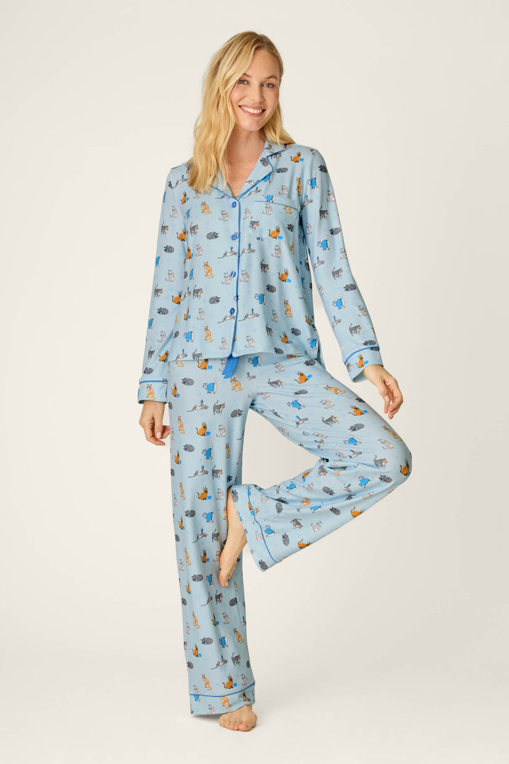 A smiling woman stands barefoot on one leg, playfully posing against a plain light background in the Hanukkatz Paws for Celebration Cat Print PJ Set by P.J. Salvage.