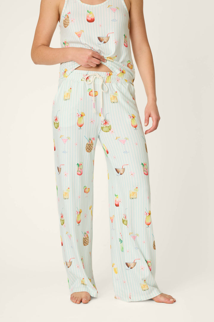 A person stands barefoot against a plain background wearing P.J. Salvage's It's Five O'clock Somewhere Cocktail Print Open Leg Pants, featuring a colorful cocktail print, drawstring waist, and relaxed fit.