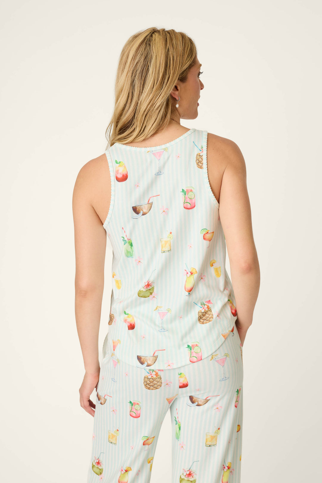 A woman with blonde hair is seen from the back wearing the P.J. Salvage It's Five O'clock Somewhere Cocktail Print Tank Top, featuring a colorful cocktail and fruit pattern on a light background.
