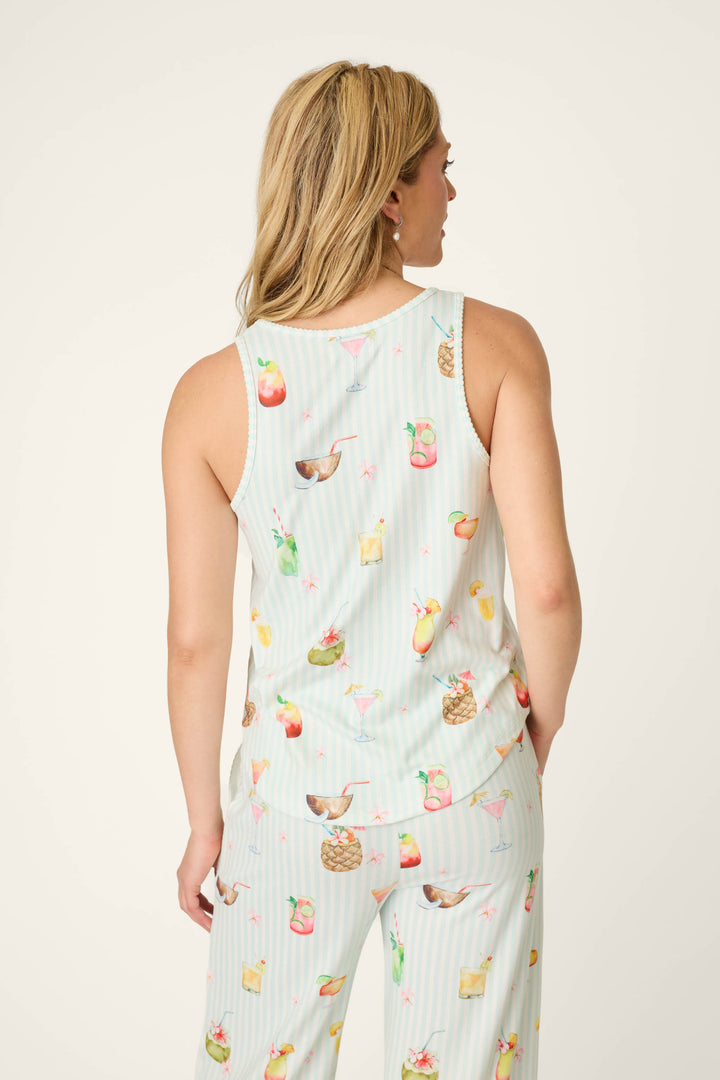 A woman with blonde hair is seen from the back wearing the P.J. Salvage It's Five O'clock Somewhere Cocktail Print Tank Top, featuring a colorful cocktail and fruit pattern on a light background.