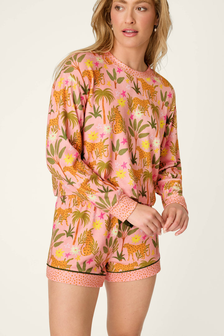 A person in the P.J. Salvage "In the Jungle Leopard Safari" Long Sleeve Top stands against a plain background, wearing the colorful jungle print pajama set and looking off to the side with a relaxed expression.