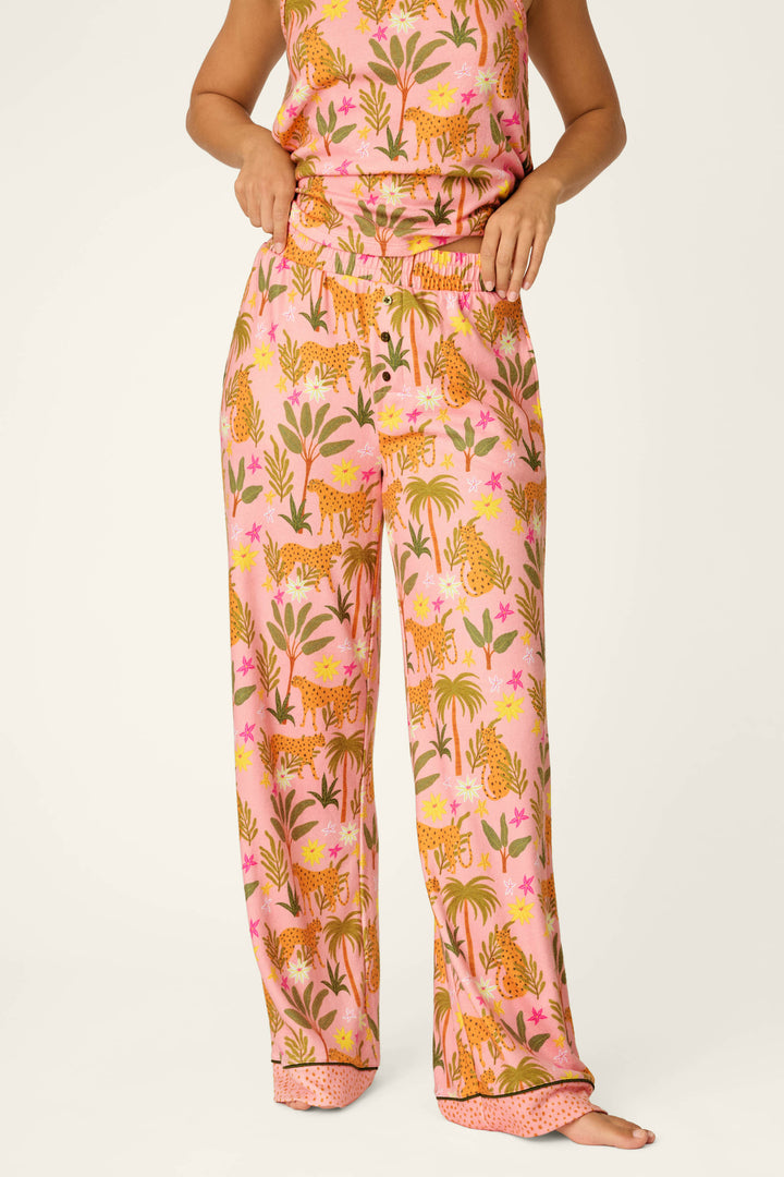 A person wears P.J. Salvage's In the Jungle Leopard Safari Open Leg Pants, featuring a vibrant jungle print with tigers, plants, and flowers. The matching soft peachy jersey top is partly visible against a plain, light background.