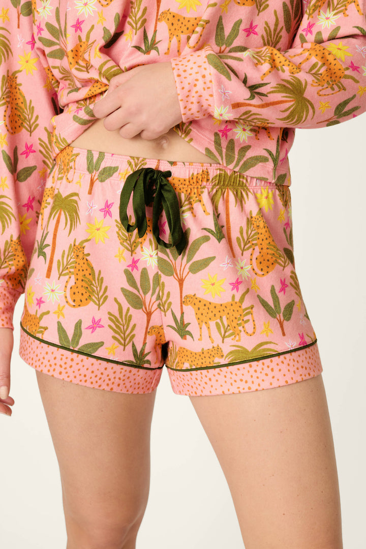 Wearing the P.J. Salvage In the Jungle Leopard Safari Short PJ Set, featuring a colorful cheetah and foliage print, black drawstring, and polka dot trim, the person stands with a hand on their hip.