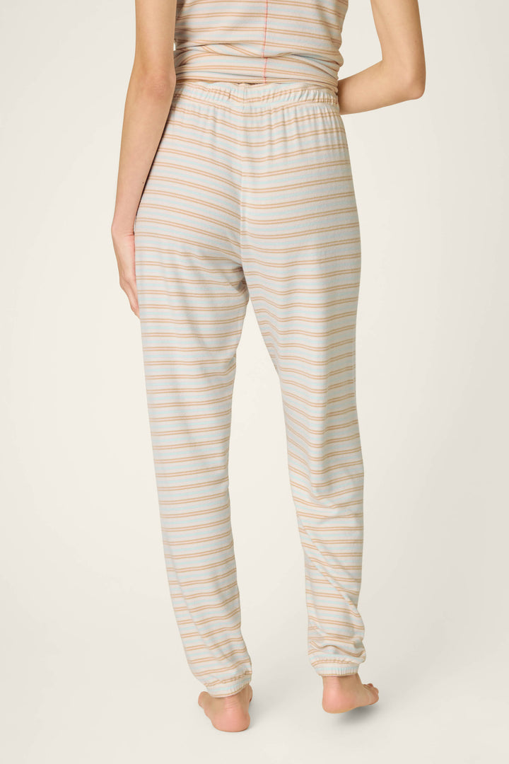 A person stands barefoot on a plain background, shown from the back, wearing P.J. Salvage's J'Adore Amour Sweetheart Stripes Lounge Pants—light-colored pajama pants featuring pastel stripes and a comfortable drawstring waist.