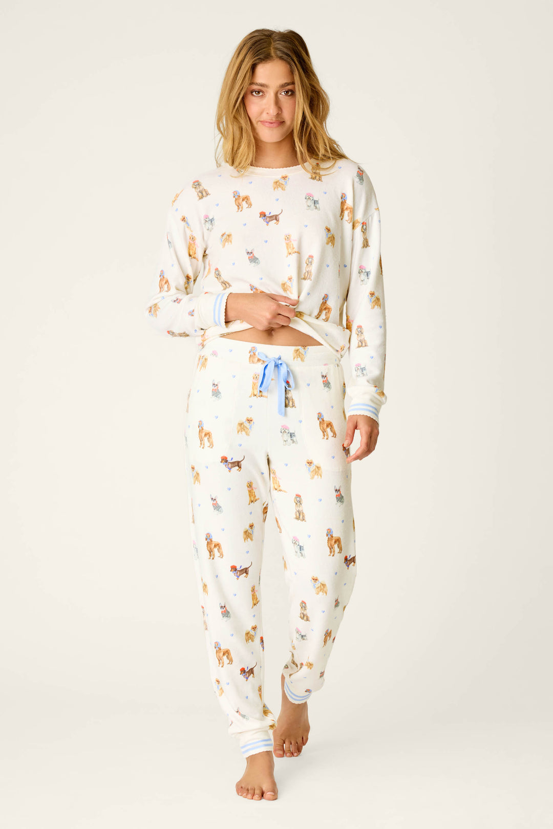 A person stands barefoot against a plain background, looking at the camera with a relaxed expression while wearing P.J. Salvage's Meet Me in Pawris Dog Print Jogger Pajama Pants.