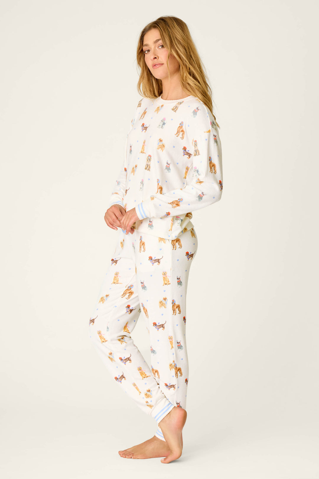 A woman stands barefoot against a plain light background, looking at the camera with a relaxed expression while wearing the P.J. Salvage Meet Me in Pawris Dog Print Long Sleeve PJ Set.